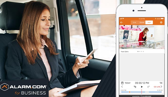 A person is sitting in a car monitoring business on smartphone using alarm.com app 