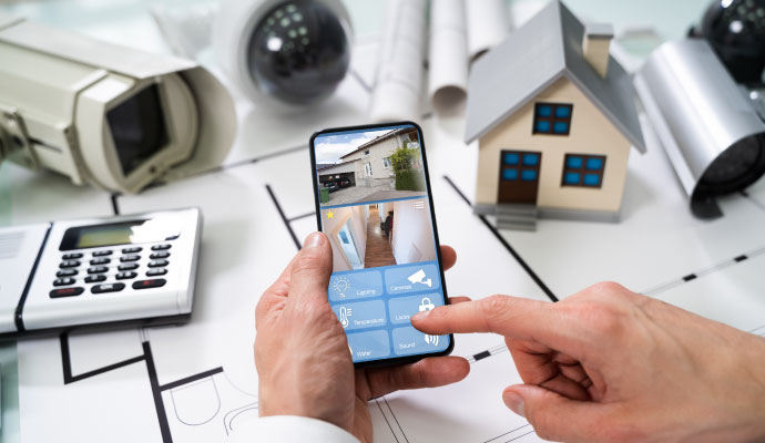 Smartphone displaying live home security camera feeds alongside house blueprints