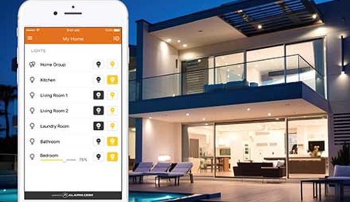 A smartphone displaying a home automation app next to a modern luxury villa at night with integrated smart lighting across multiple rooms