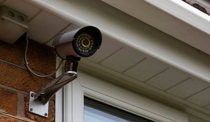 Wired outdoor security camera mounted on exterior brick wall with cable connection